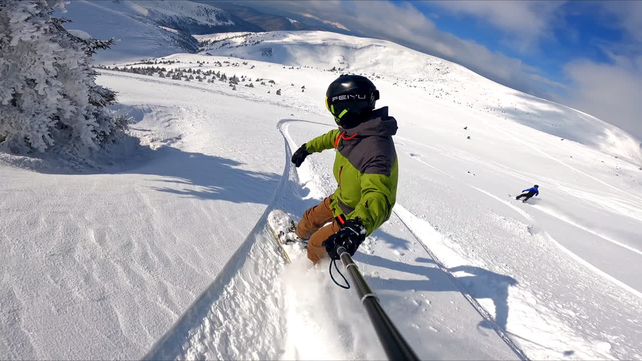 Male snowboarder taking selfie as he's going down the slope. Active and fun time spending in the mountains in winter.