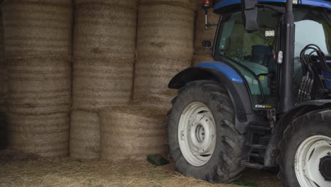 medium shot of a blue tractor parked infront of hay balls