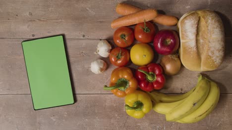 foto de estudio superior de la mano recogiendo alimentos frescos básicos con tableta digital de pantalla verde en la superficie de madera 3