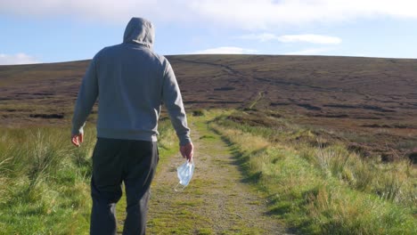 Kranker-Mann-Lässt-Seine-Gesichtsmaske-Fallen,-Während-Er-Auf-Dem-Bergweg-In-Wicklow-Mountains,-Irland-Geht---Totale-Aufnahme