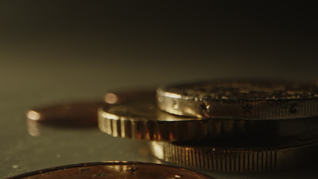 Macro pan of a stack of Euro coins in a studio setting. A variety of nickels, single euro's and 2 euro coins are cinematically lit on a white background