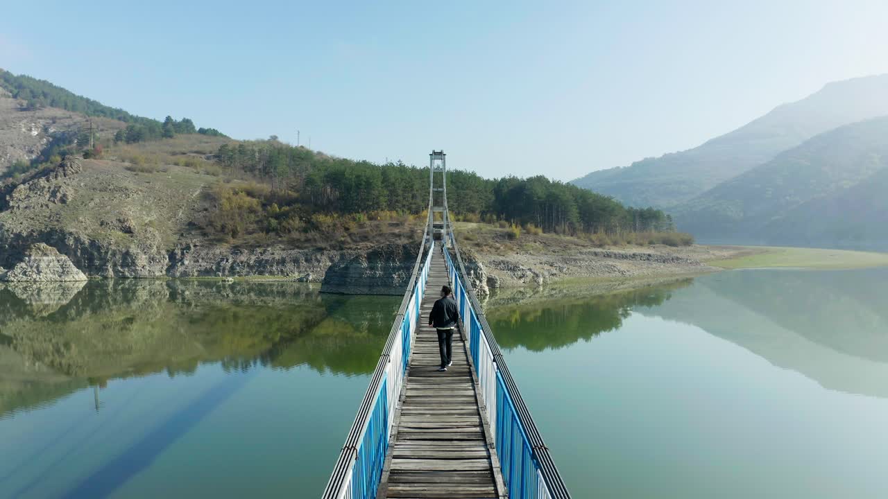 vista aérea de un hombre caminando sobre un puente sobre la presa de studen kladenec en bulgaria, con montañas en el fondo