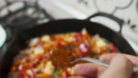 enfoque de cerca en una cuchara con especias rojas puestas en una mezcla de verduras dentro de una sartén caliente