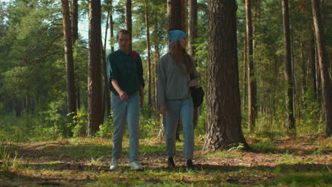 two sisters walking through a sunlit forest, one wearing red backpack with cloth and the other with blue headscarf, as sunlight filters through trees and reflects gently on their faces