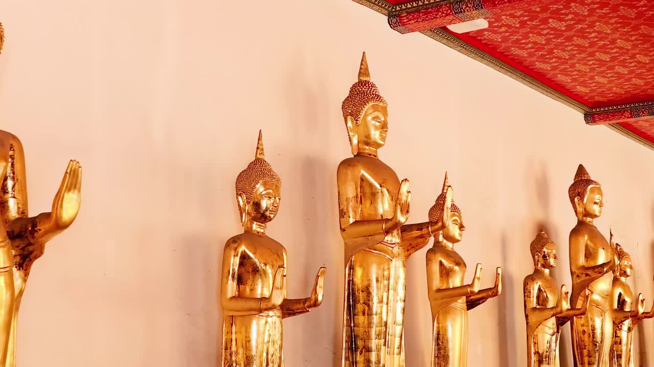 A row of golden Buddha statues beneath an ornate red ceiling, showcasing intricate craftsmanship and serene expressions.