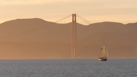 bateau à voile passant le pont du golden gate au coucher du soleil