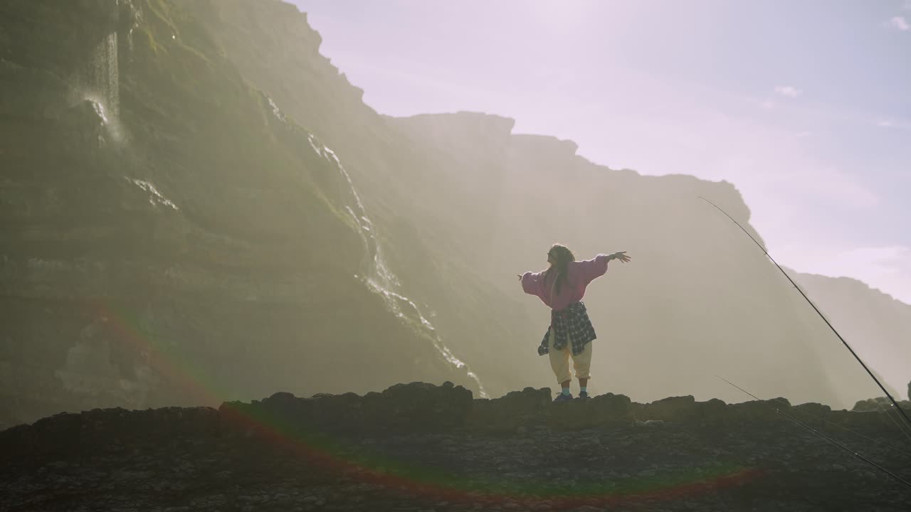 Giovane donna che allunga le braccia su una scogliera nebbiosa con cascata
