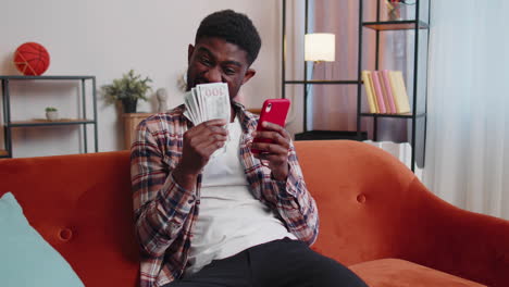 smiling happy young man counting money cash and use mobile phone calculate domestic bills at home