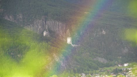 Arco-Iris-Frente-A-La-Ruina-Del-Antiguo-Castillo-Y-Un-Bosque-Con-Un-Pueblo-Al-Fondo-En-Tirol,-Austria