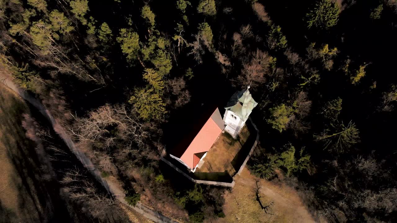 Drone flying about the church in Slovenia. Camera going from low to high in the sky. Looking down on the church nested between the trees.