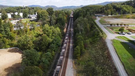 Aerial-flyover-long-line-of-train-cars-sitting-stationary-on-train-tracks-during-the-summer