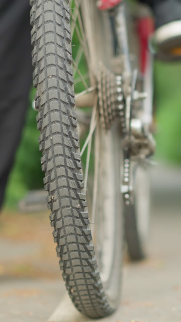 primer plano de alguien girando el pedal de su bicicleta hacia atrás mientras está de pie en un camino pavimentado, la rueda de la bicicleta y el pedal están en foco, mientras que la vegetación en el fondo está borrosa