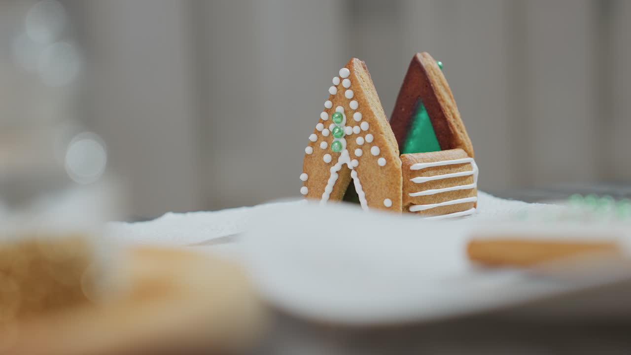 보케 효과로 둘러싸인  가죽 종이 위에 자랑스럽게 서 있는 초록색과 색의 아이싱으로 장식된 집 모양의 쿠키의 클로즈업