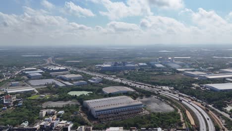 drone view of chennai's industrial landscape. a major highway connects vast factories and commercial buildings. ponds and distant rural areas offer contrast. sriperumbudur sipcot industrial park