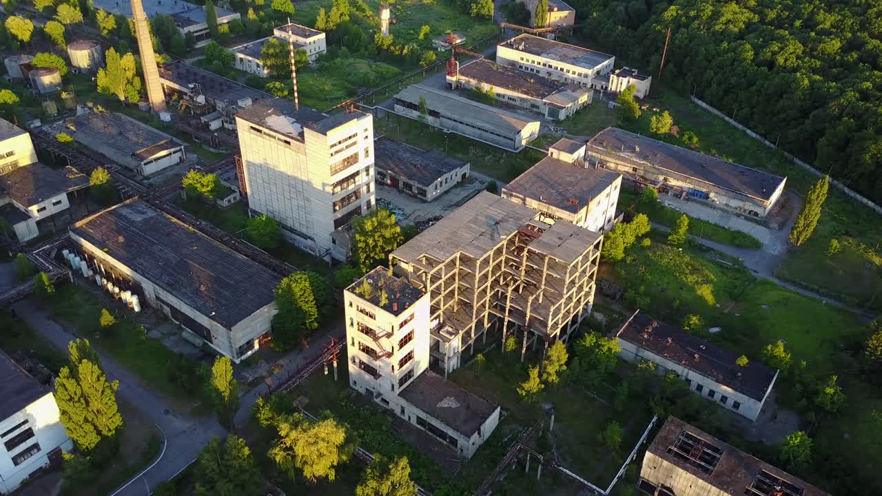 Old Ruinous Factory At Sunset. Discard old industrial factory exterior with buildings and smokestack