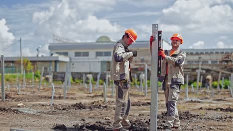 construction the solar power plant. engineering team in orange helmets and uniform working on installing metal basis for future solar farm.