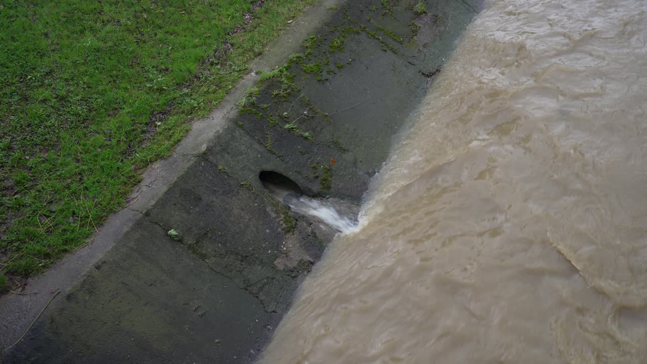 Culverts drain murky city water into overflowing river after heavy rain