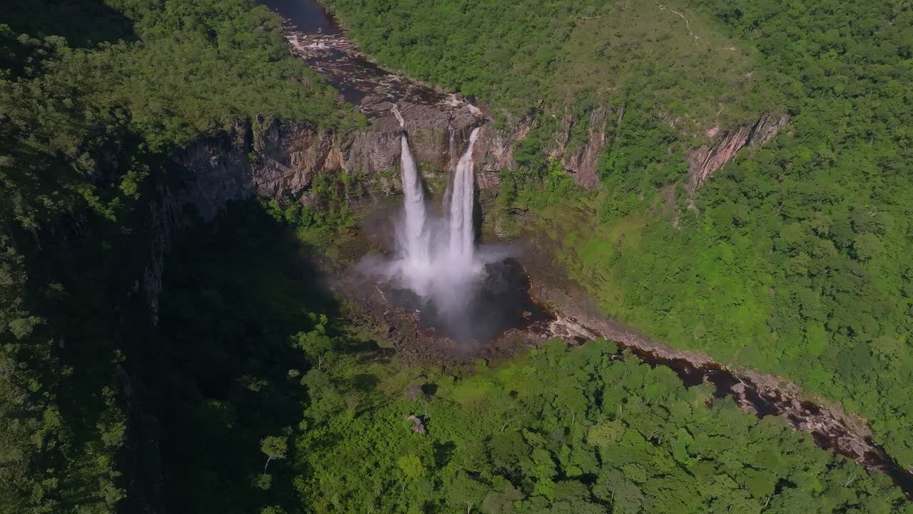 Aerial view capturing the Cachoeira dos Saltos waterfall cascading into a natural pool, surrounded by lush vegetation in Chapada dos Veadeiros National Park, Unesco world heritage, drone reveal.