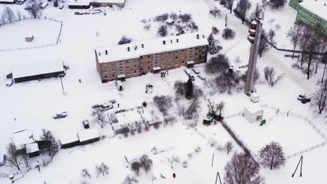 Apartment-building-in-snow-covered-rural-village-landscape,-aerial-view