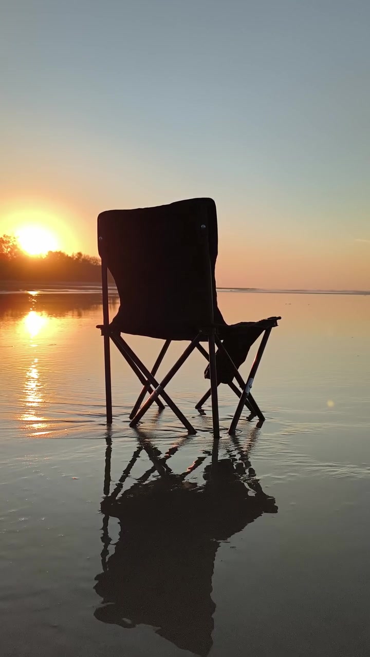 Silhouette d'une chaise pliante sur une plage au coucher du soleil