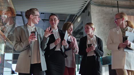 Front-view-of-a-group-of-confident-businesswoman-colleagues-walking-along-the-corridor-in-the-office-and-talking-about-their-current-issue-and-affair.-Group-of-confident-businesswoman-colleagues-in-business-clothes