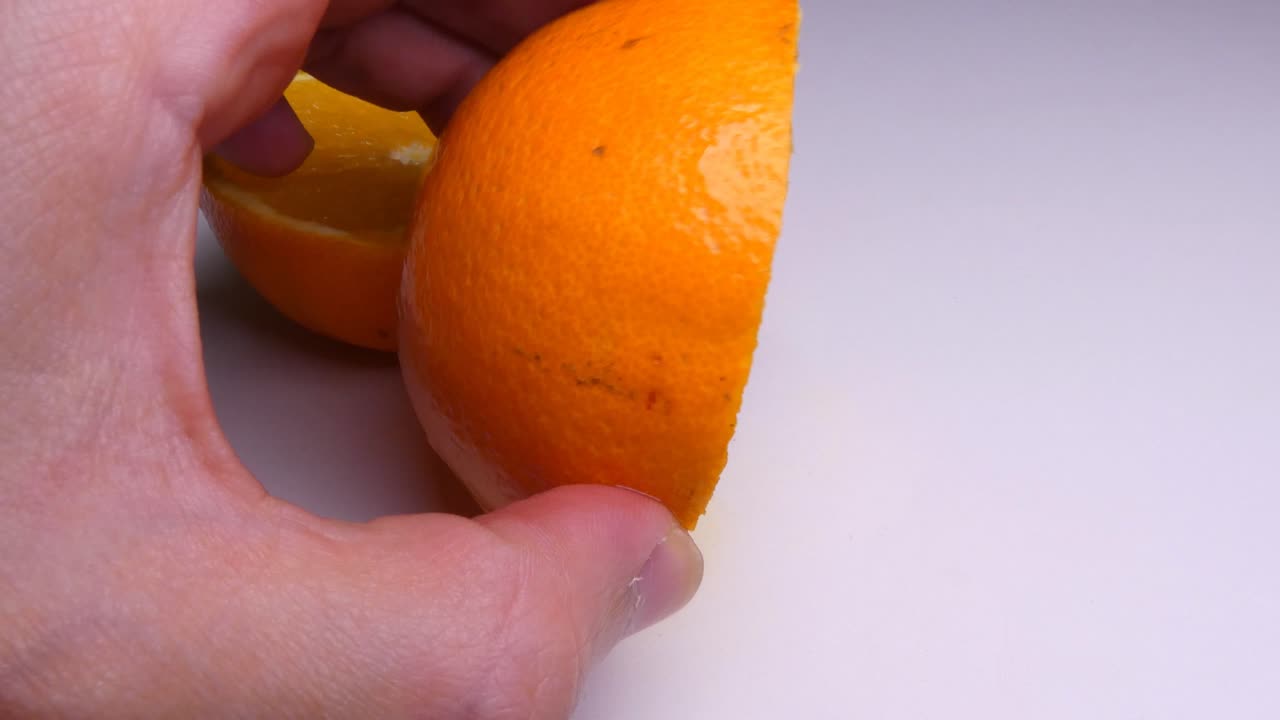 An orange sliced in half on a white background. A hand comes into frame and touches and squeezes the orange.