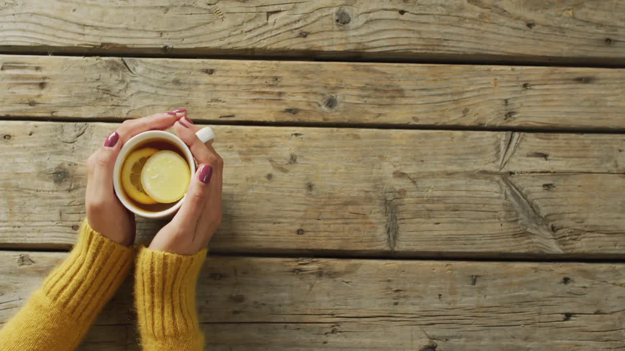 Video of hands of caucasian woman holding mug with tea and lemon on wooden surface