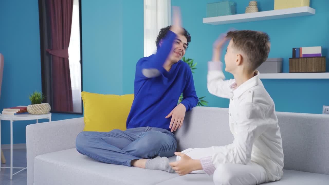 Two adult children sitting happily on the sofa and congratulating each other.