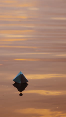paper boat on evening water. white origami boat floating alone on light waves on water surface at sunset. vertical video