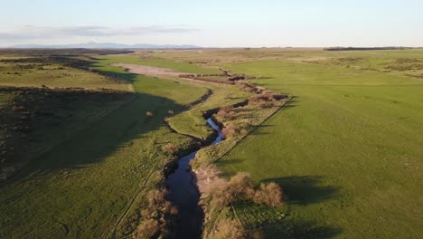 Aerial-shot-with-sunset-light-of-small-creek-going-through-rural-fields