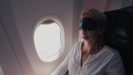 a young woman with a dark bandage in her eyes sleeps in the cabin of a passenger aircraft traveling