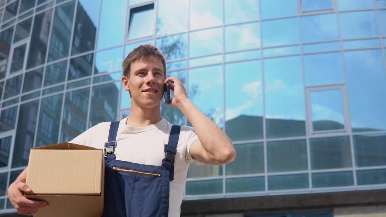 transporte y entrega de bienes fabricados. entrega de bienes a la oficina. un trabajador de entrega sostiene una caja en sus manos y habla en un teléfono celular y descubre la dirección de entrega