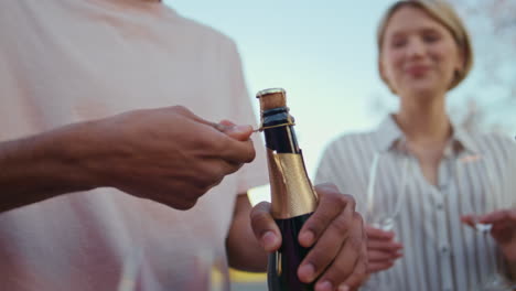 man hands opening champagne bottle party closeup. friends holding glasses