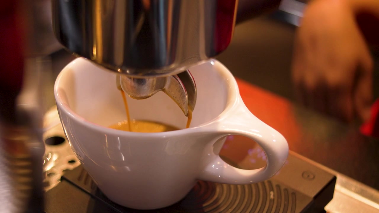 Primer plano de crema de espresso dorada fluyendo en una taza de café con leche blanca en una máquina de café, cafetería de especialidad.