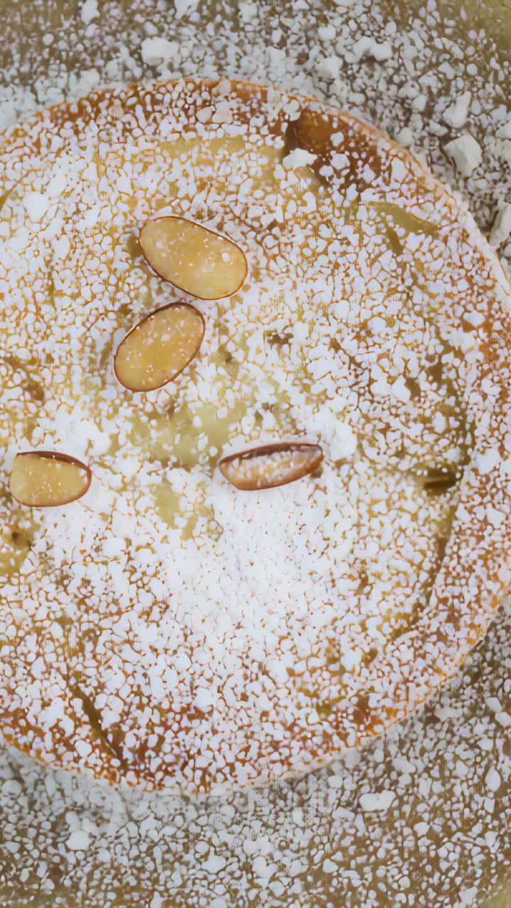 Vertical video: Pulling camera toward tart on plate at home to show sugar dust and 3 almond slices