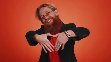 smiling redhead man makes heart gesture demonstrates love sign expresses good feelings and sympathy