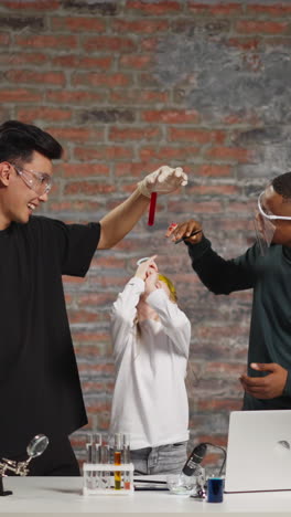 joyful asian and african-american chemists hold test tube above girl student shooting video for blog at online fun science lesson in improvised classroom