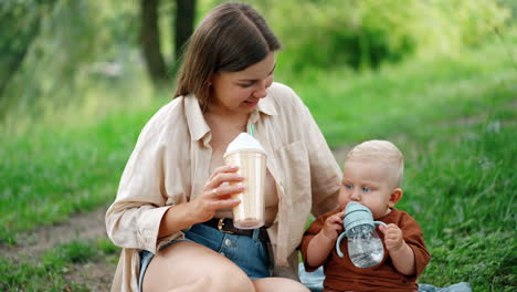 mom and her little son sit on the plaid outdoors on summer day. mother and child drink water.