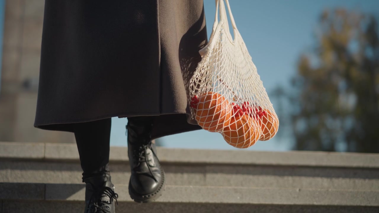 Persona che scende scale di pietra trasportando arance in una borsa a rete