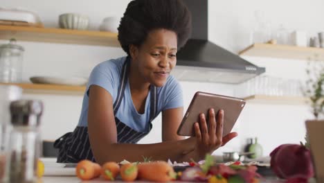 Glückliche-Afroamerikanische-Frau,-Die-In-Der-Küche-Das-Abendessen-Mit-Einem-Tablet-Zubereitet