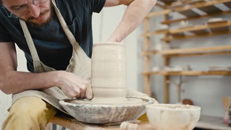 close up of male potter forming handmade vase on pottery wheel at studio, slow motion