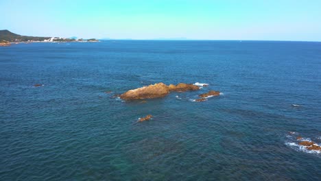 flying over seascape, towards rocky reef on sunny day