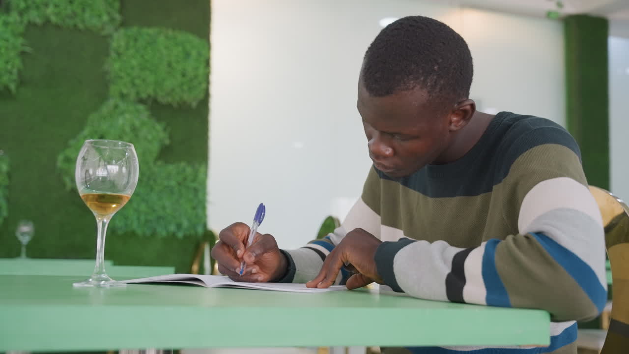 Student working on application form. Person filling out form in stylish cafe setting. Person focused on completing paperwork in vibrant modern cafe atmosphere with decorative moss wall