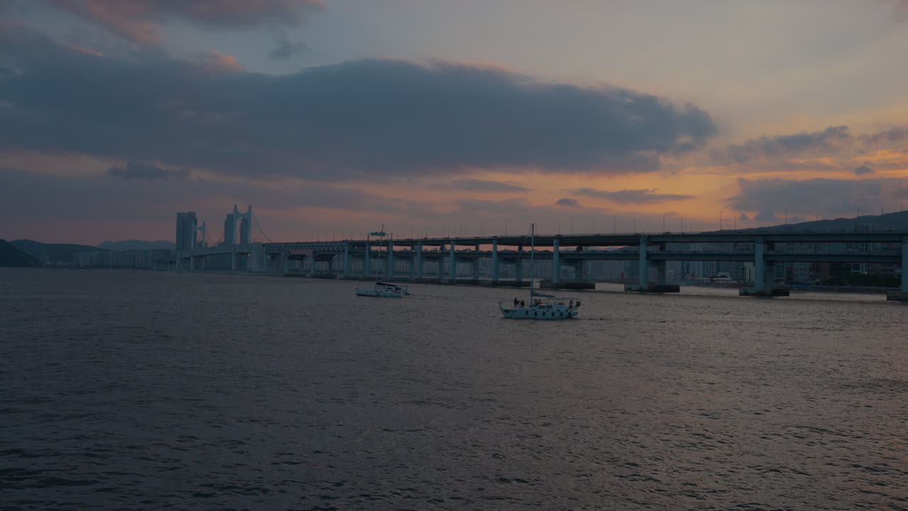몇몇 항해 요트는 푸른 시간에 부산에서 해가 지는 동안 극적인 보라색 하늘 구름과 함께 gwangju 다리 에서 바다를 여행합니다.