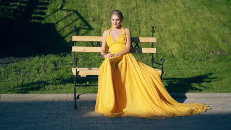 Young-beautiful-girl-in-a-beautiful-yellow-evening-dress-sitting-on-a-bench