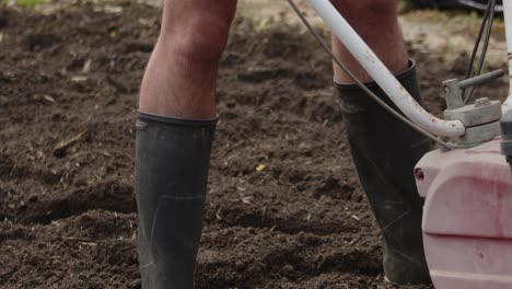 jardinero con botas de goma cultivando el paisaje del jardín con rotavator