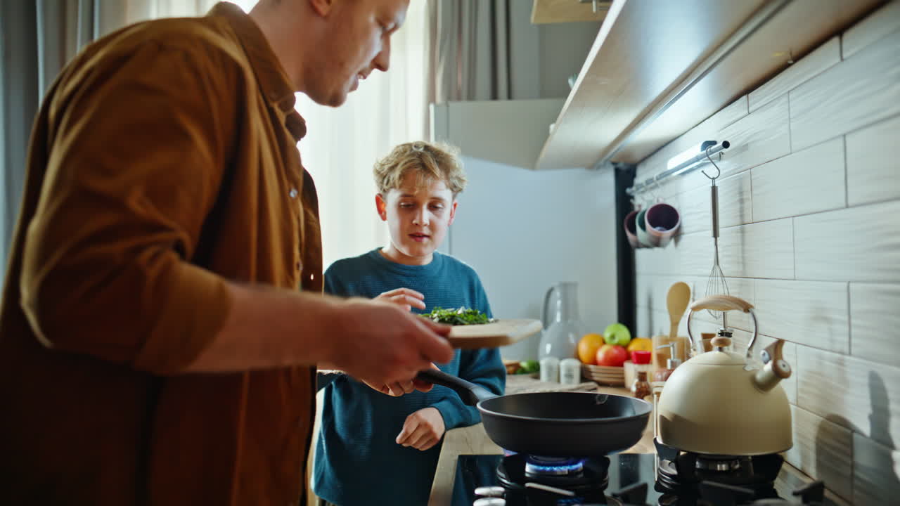 Vater und Sohn braten Omelett am heimischen Herd, genießen die gemeinsame Zeit. Nahaufnahme.