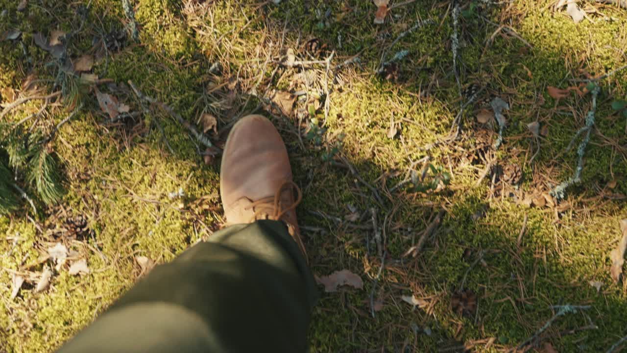 숲의 모스 위를 고 있는 갈색 부츠를 입은 남성의 다리의 면. 느린 동작 비디오