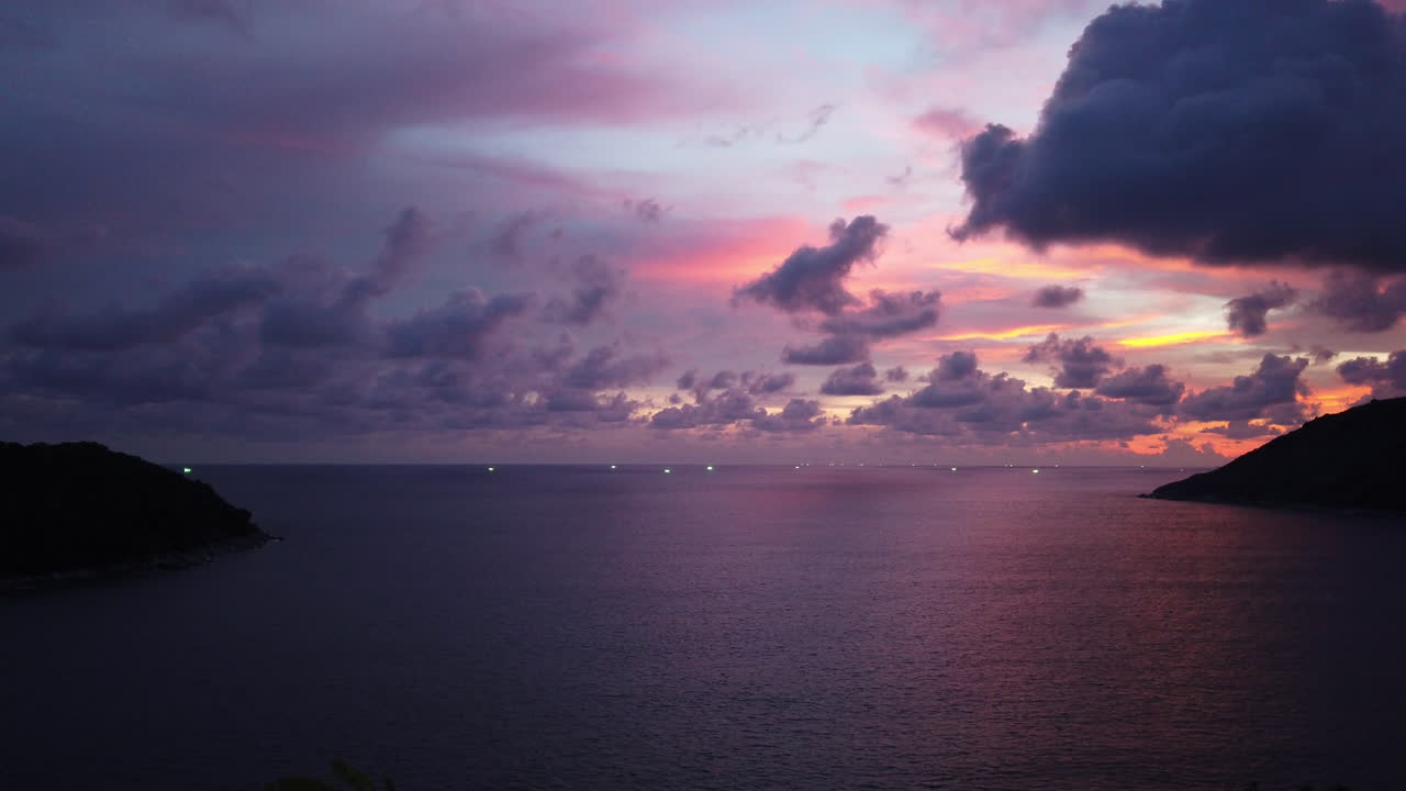 scatto panoramico bloccato in un ampio lasso di tempo di un tramonto tropicale dopo una giornata monsonica piovosa con cielo drammatico dorato, viola e blu e paesaggio nuvoloso sopra una tranquilla vista elevata sulla baia dell'oceano
