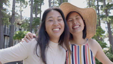 Felices-Amigas-Asiáticas-Con-Gafas-De-Sol-Paradas-Y-Sonriendo-En-Un-Jardín-Soleado,-Cámara-Lenta